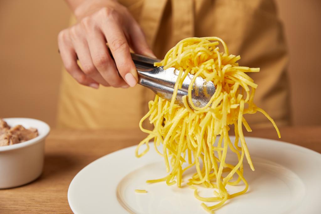 oříznutý snímek ženy uvedení špagety na talíři s kleštěmi - Fotografie, Obrázek