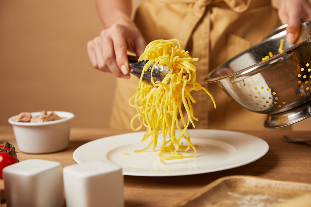 cropped shot of woman putting spaghetti on plate from colander - Photo, Image