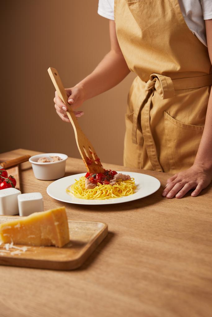plan recadré de la femme dans le tablier mettre des pâtes dans l'assiette sur la table en bois
 - Photo, image