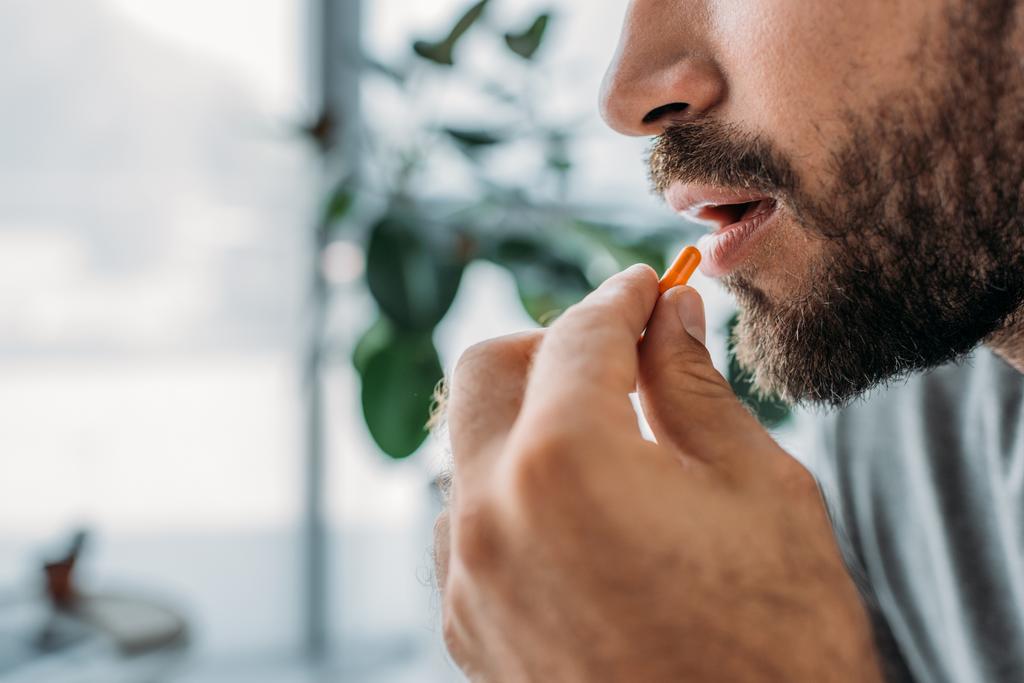 обрізаний знімок бородатого чоловіка тримає таблетку біля рота
 - Фото, зображення