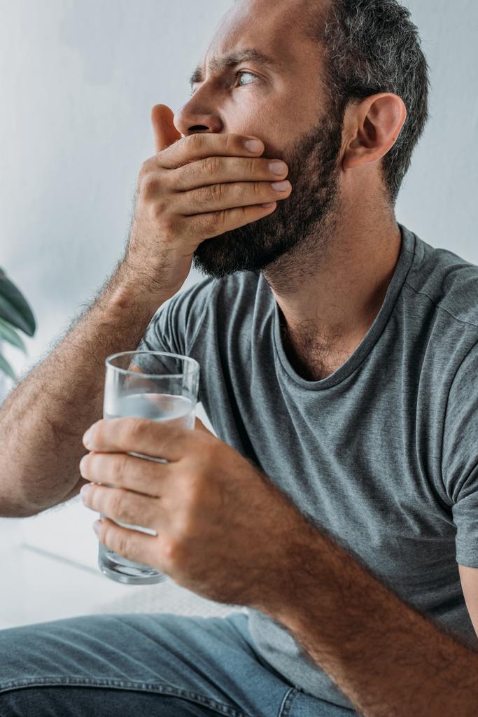 бородатий чоловік тримає склянку води і приймає ліки
 - Фото, зображення