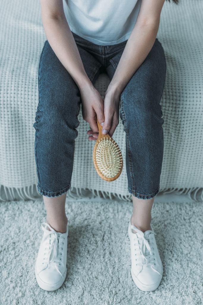 cropped shot of young woman holding hairbrush and sitting on couch, hair loss concept - Photo, Image