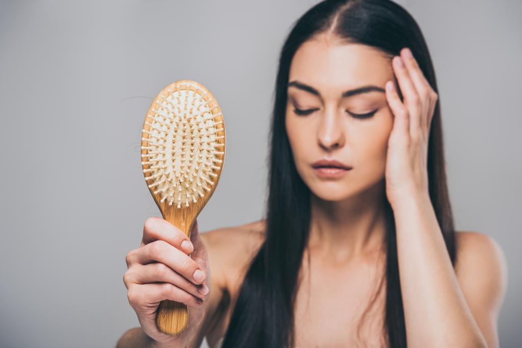 stressed brunette woman with closed eyes holding hairbrush isolated on grey, hair loss concept - Photo, Image