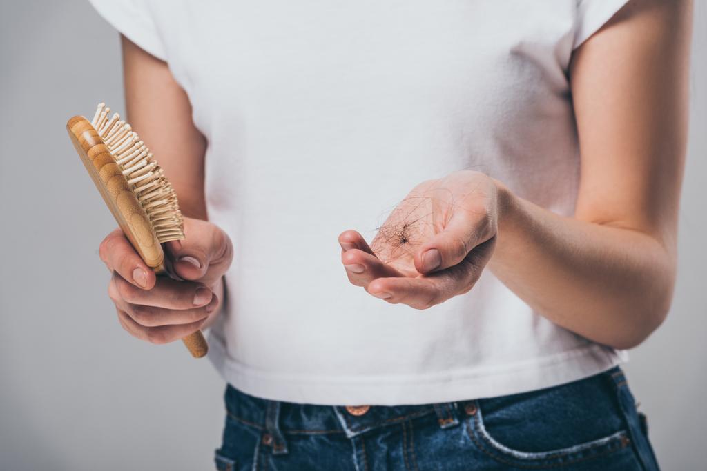 cropped shot of woman holding hairbrush and fallen hair isolated on grey, hair loss concept - Photo, Image