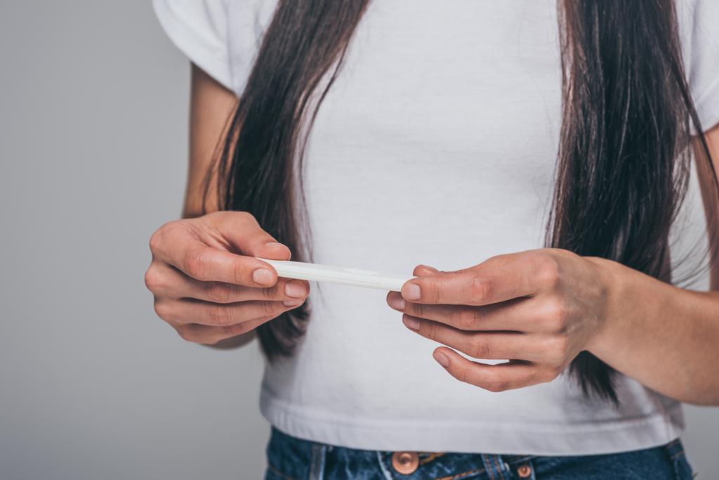 обрезанный снимок молодой брюнетки с тестом на беременность, изолированный на серой
 - Фото, изображение