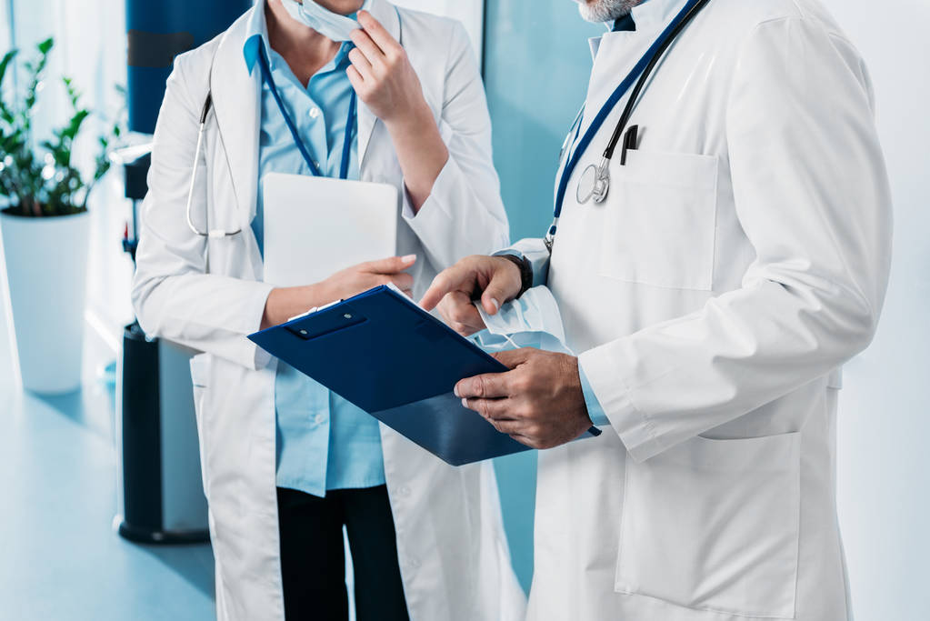 Teilansicht eines männlichen Arztes, der auf Klemmbrett zu Ärztin zeigt, mit digitalem Tablet im Krankenhausflur  - Foto, Bild