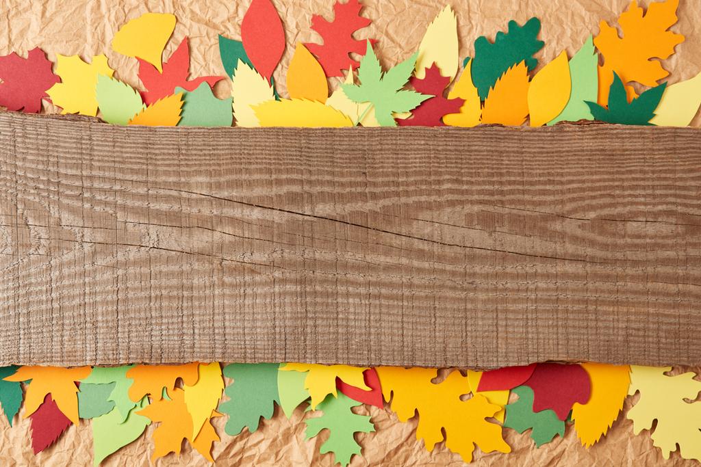 top view of wooden plank and colorful paper leaves arrangement on crumpled paper backdrop - Photo, Image