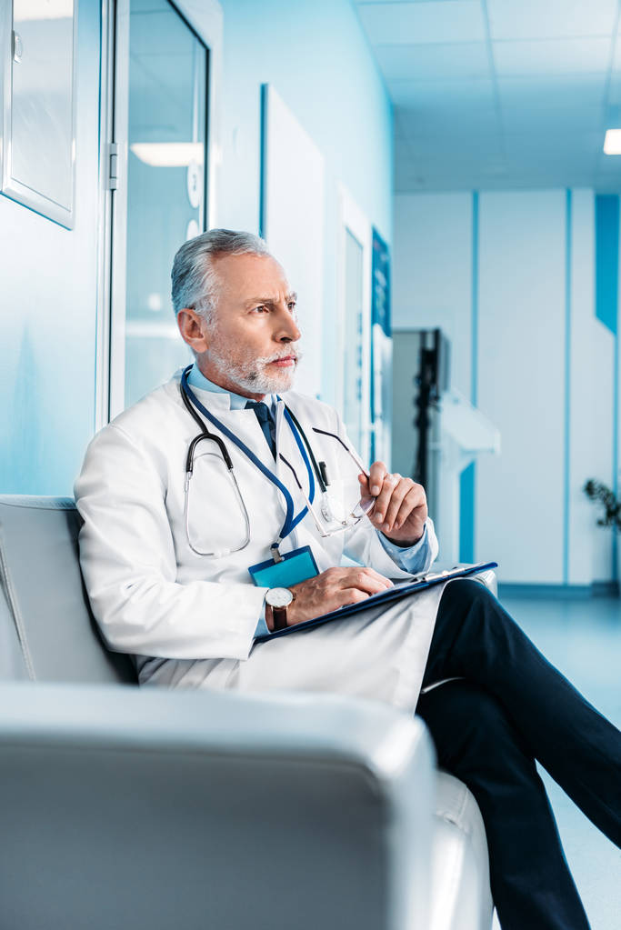 cílené starší mužské doktor s schránky drží sedící na gauči v nemocniční chodbě  - Fotografie, Obrázek