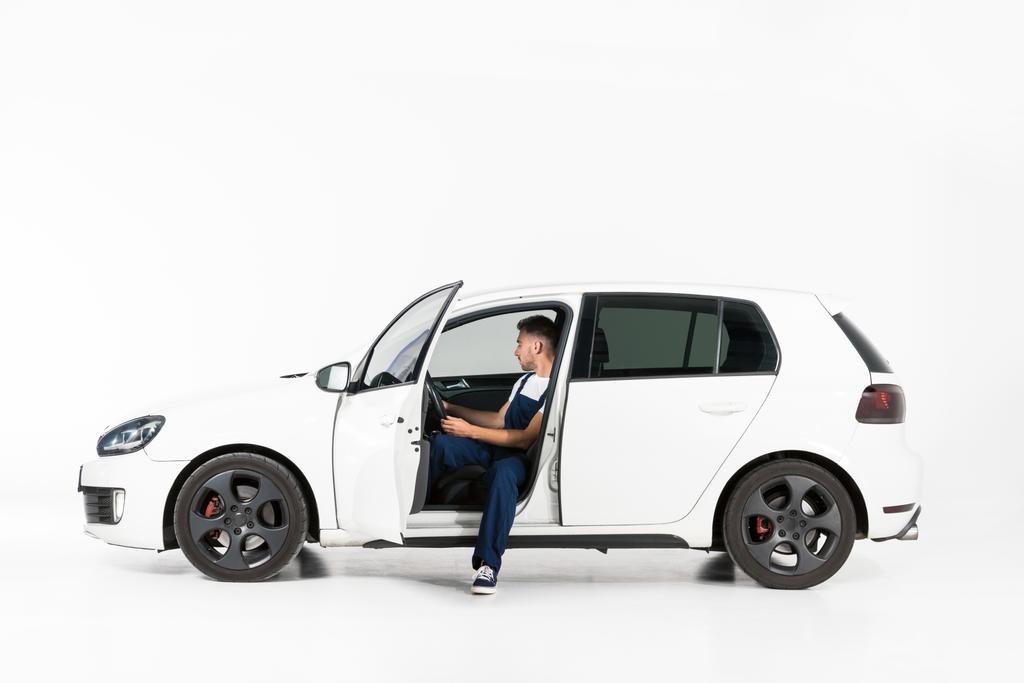 boční pohled hezký auto mechanik sedí v autě na bílém - Fotografie, Obrázek