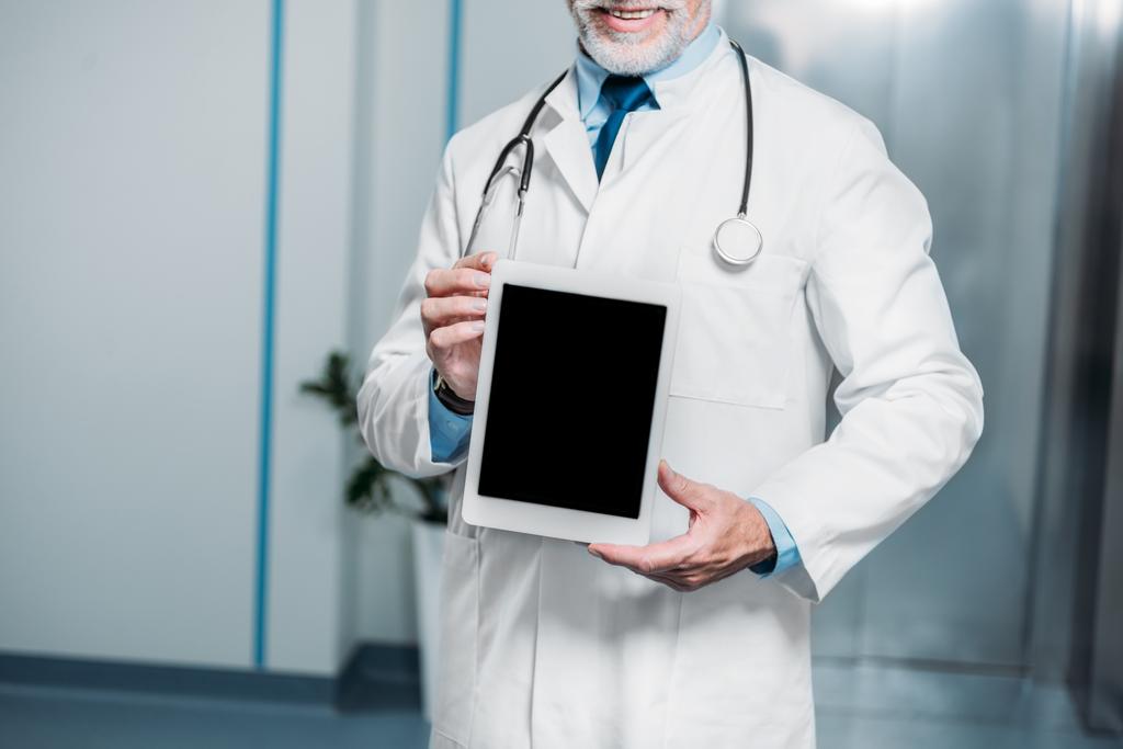 gedeeltelijke weergave van volwassen mannelijke arts met de stethoscoop over hals digitale tablet met leeg scherm tonen in ziekenhuis  - Foto, afbeelding