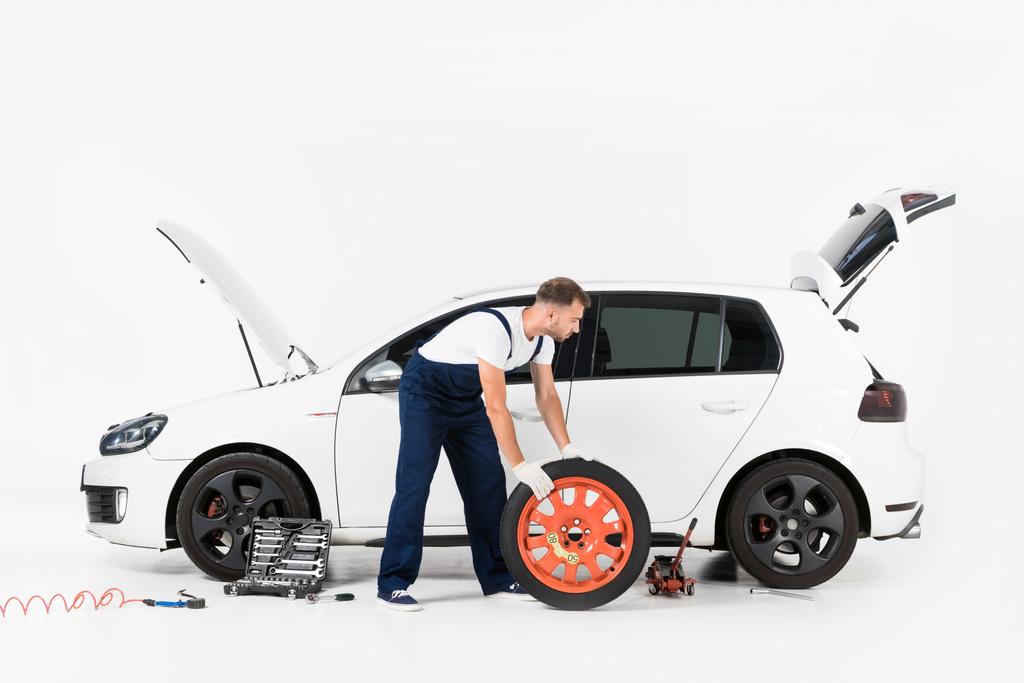 boční pohled na Automechanika v modré uniformě měnící se auto pneumatiky na bílém - Fotografie, Obrázek