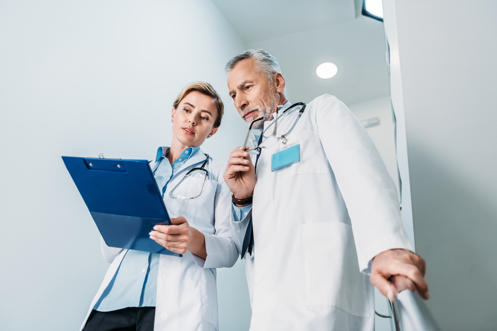 visão de baixo ângulo de médico do sexo feminino mostrando prancheta para colega do sexo masculino em escada no hospital
  - Foto, Imagem