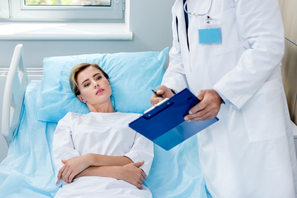 vista parcial del médico masculino con estetoscopio sobre el cuello señalando el portapapeles al paciente femenino en la habitación del hospital
  - Foto, Imagen