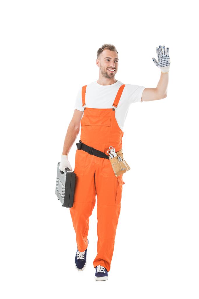 handsome auto mechanic in orange uniform holding toolbox and waving hand isolated on white - Photo, Image