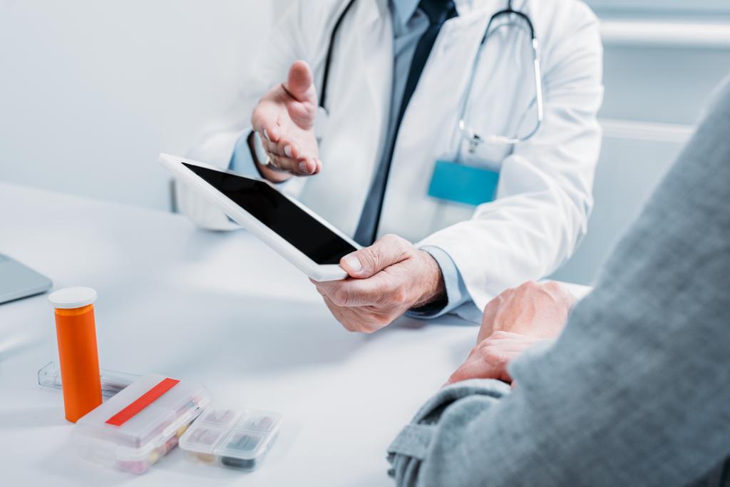 częściowy widok lekarza Mężczyzna, wskazując na cyfrowy tablet z pustego ekranu aby pacjentka w tabeli w biurze  - Zdjęcie, obraz
