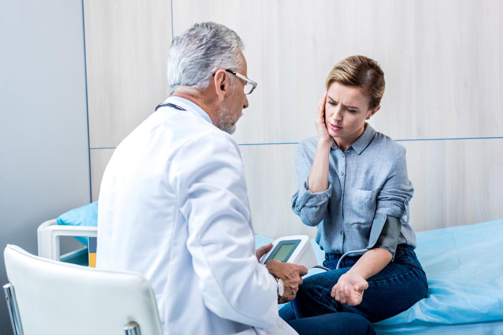 Rückansicht eines männlichen Arztes mit Stethoskop, das den Druck einer Patientin mit einem Tonometer im Krankenhauszimmer misst - Foto, Bild