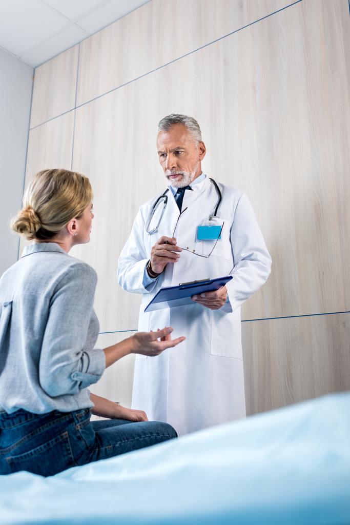 vue arrière du patient féminin gesticulant à la main et parlant au médecin masculin avec presse-papiers dans la chambre d'hôpital
 - Photo, image