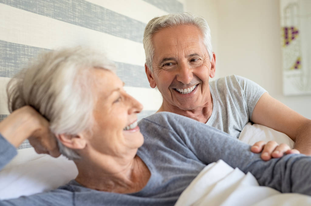 Couple âgé souriant couché sur le lit par une matinée ensoleillée. Heureux vieil homme couché près de sa femme au lit. Couple mature s'amuser ensemble dans la chambre
. - Photo, image