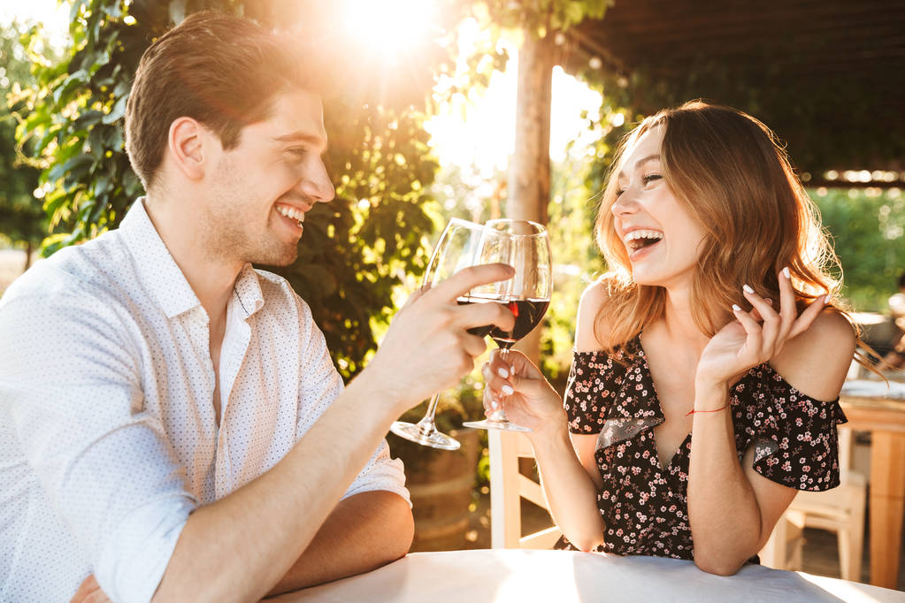 Outdors birbirleriyle konuşurken içme şarap gözlük tutan Park çıkarak kafede oturan genç sevgi dolu çift resmini. - Fotoğraf, Görsel