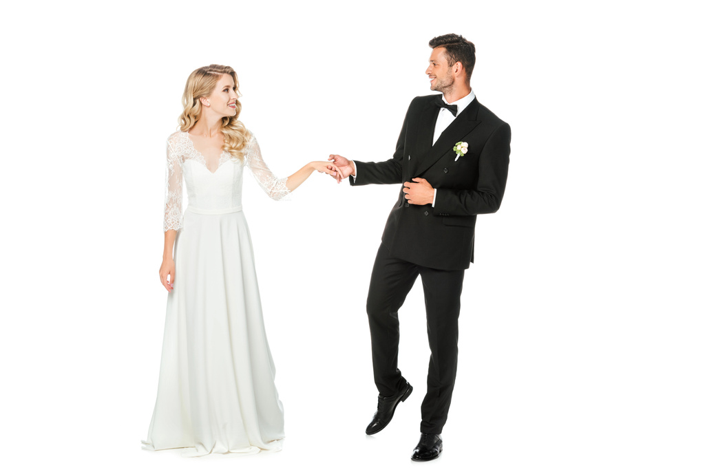 smiling young bride and groom holding hands and looking at each other isolated on white - Photo, Image