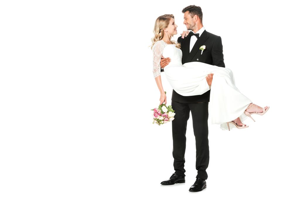 šťastný mladý ženich nese svou nevěstu izolované na bílém - Fotografie, Obrázek