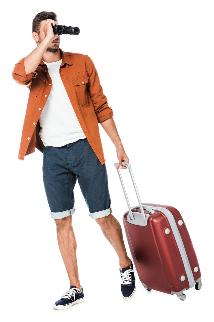 Gelukkig jonge man met verrekijker en bagage wandelen en op zoek weg op wit wordt geïsoleerd - Foto, afbeelding