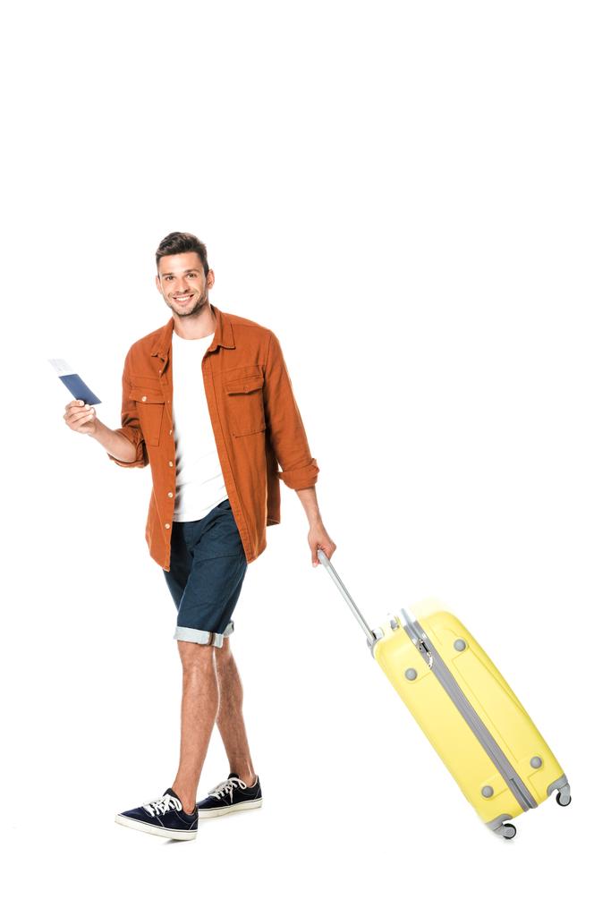joven feliz con equipaje y billete de avión caminando y mirando a la cámara aislada en blanco
 - Foto, imagen