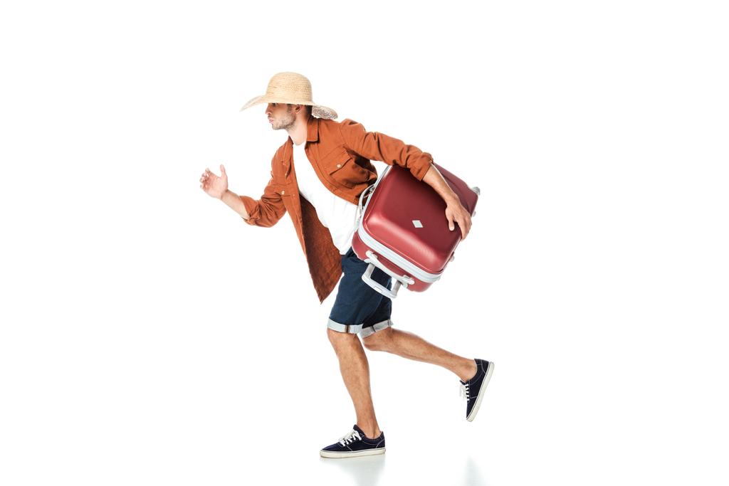 vista lateral del turista en sombrero de paja corriendo con bolsa de viaje aislada en blanco
 - Foto, Imagen