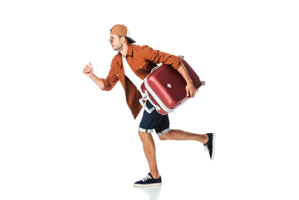 vista lateral del hombre guapo corriendo con el equipaje aislado en blanco
 - Foto, Imagen