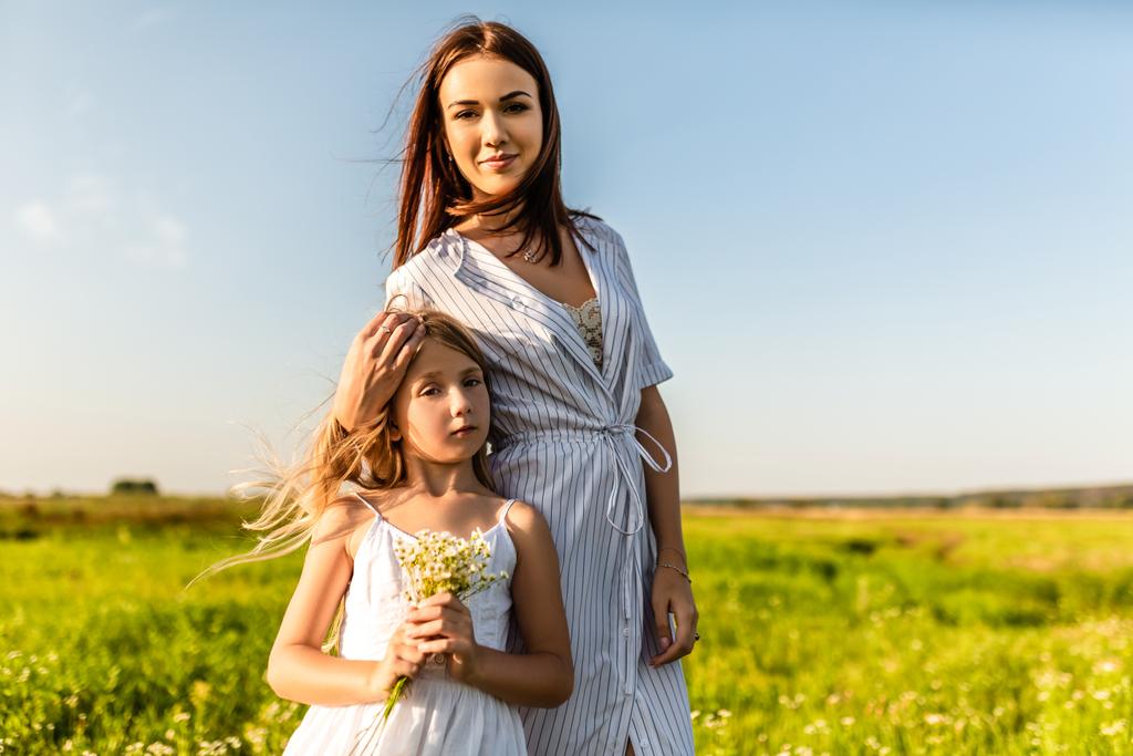 mother and daughter in white dresses looking at camera together in green field - Photo, Image