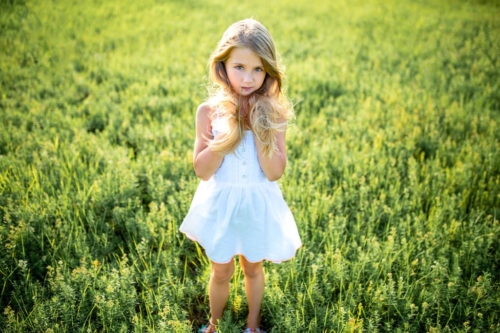 mignon petit enfant en robe blanche posant dans le champ vert et regardant la caméra
 - Photo, image
