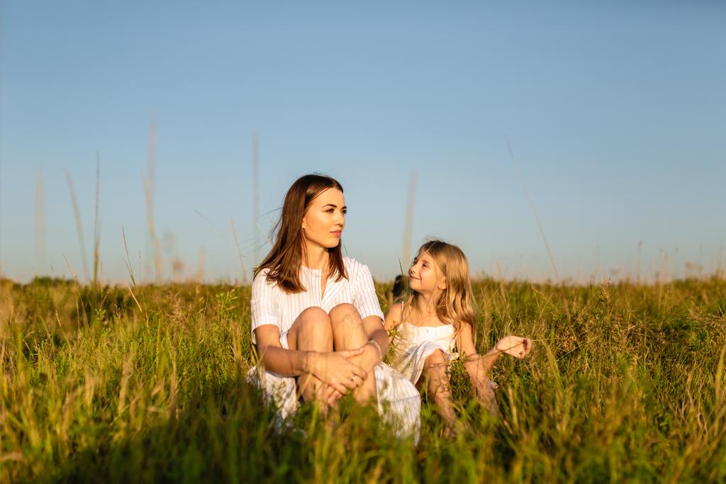 madre e figlia seduti su erba verde al tramonto e chiacchierando
 - Foto, immagini