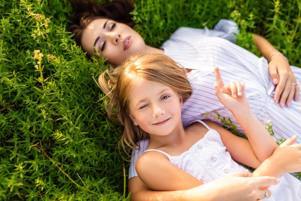 happy mother and daughter relaxing while lying in flowery meadow - Photo, Image