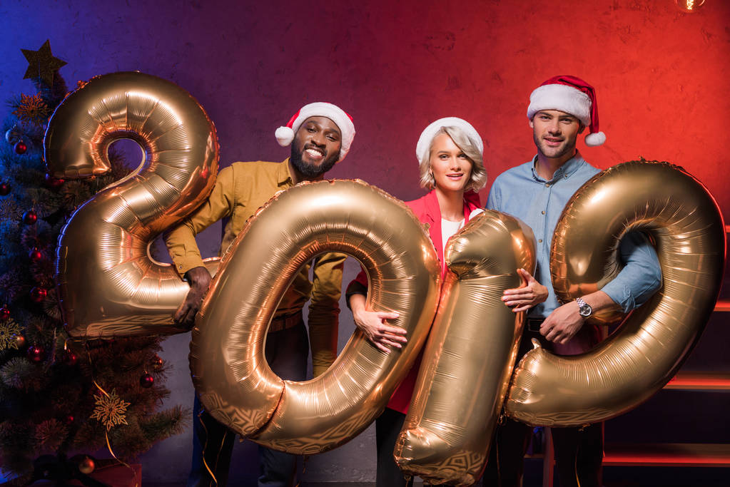 sonrientes empresarios multiculturales celebrando globos 2019 en la fiesta corporativa de año nuevo
 - Foto, Imagen
