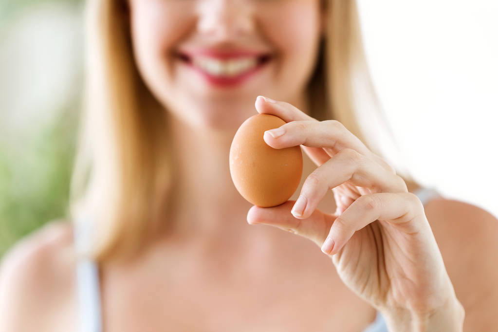 Tiro de hermosa mujer joven mostrando huevo chiken marrón en casa
. - Foto, imagen