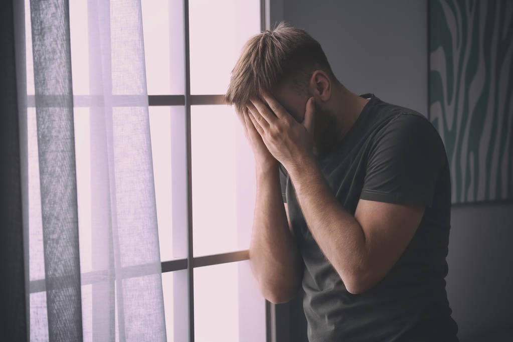 Депресивний молодий чоловік біля вікна вдома
 - Фото, зображення