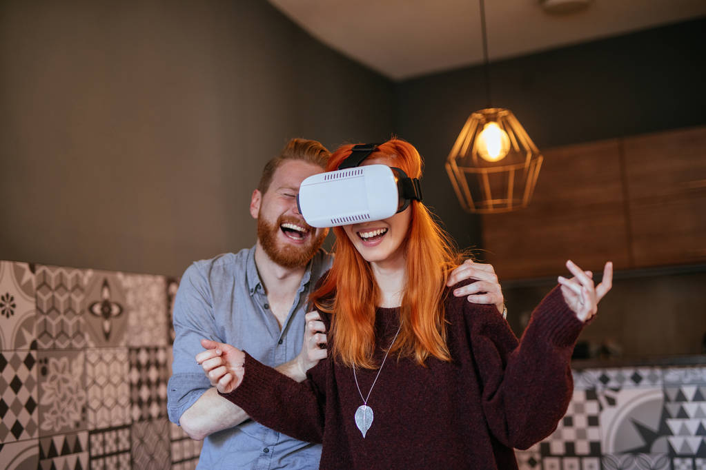 Νεαρό ζευγάρι Έχοντας διασκέδαση στο σπίτι με το σετ κεφαλής εικονικής πραγματικότητας. - Φωτογραφία, εικόνα