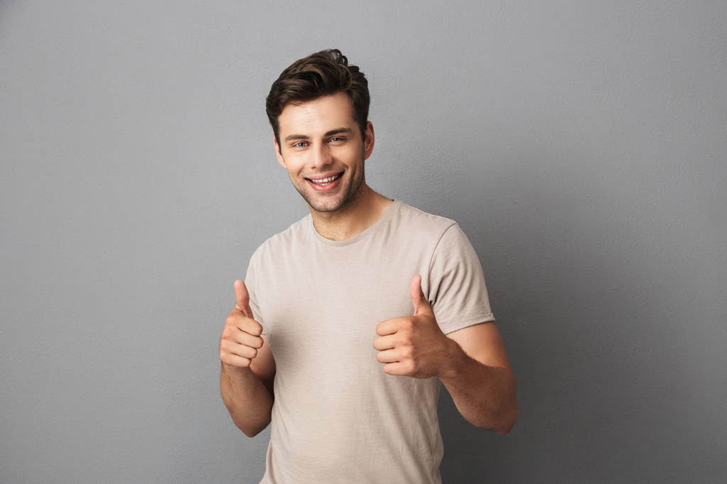 Εικόνα ελκυστική ανθρώπου 30s σε t-shirt προβολή μπράβο με χαρούμενο χαμόγελο που απομονώνονται σε γκρίζο φόντο - Φωτογραφία, εικόνα