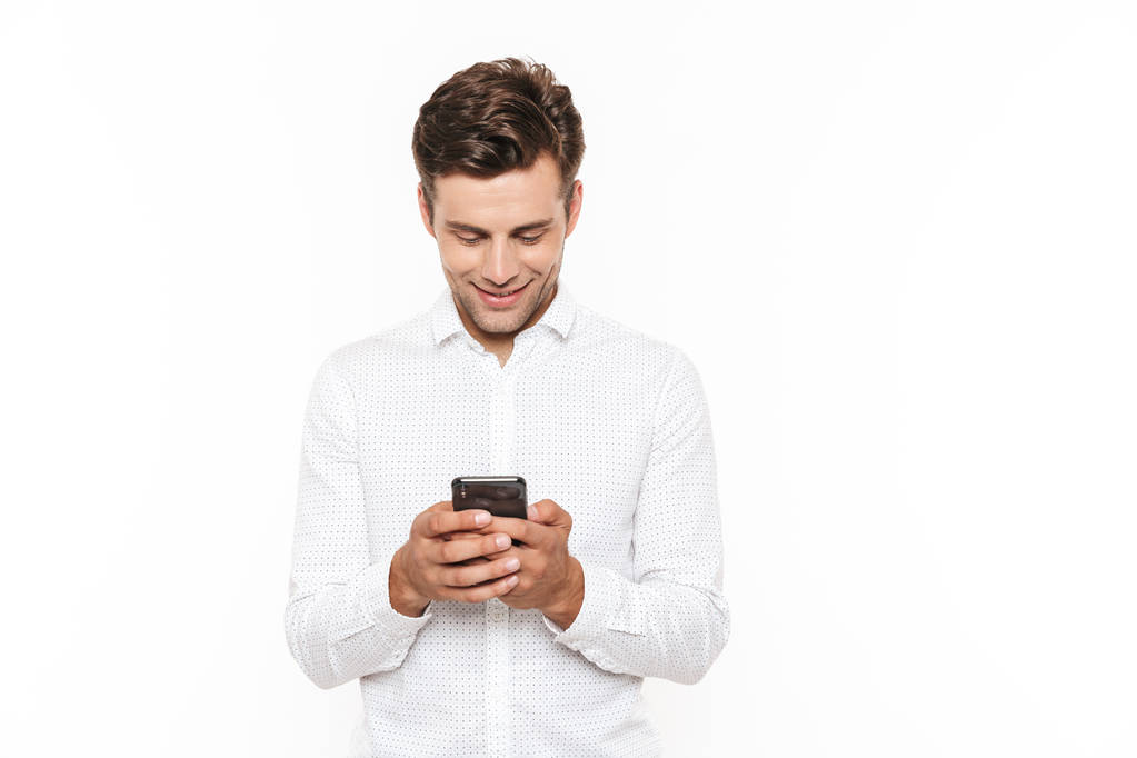 Jeune homme avec des cheveux bruns courts bavarder ou dactylographier message texte avec smartphone isolé sur fond blanc
 - Photo, image