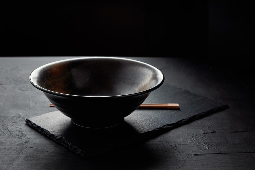 vergrote weergave van de lege kom en eetstokjes op zwarte leisteen bord - Foto, afbeelding