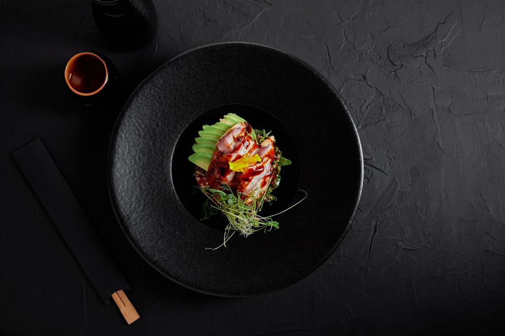Blick von oben auf köstliche traditionelle japanische Gerichte mit Meeresfrüchten, Avocado und Kräutern auf schwarzem Teller - Foto, Bild