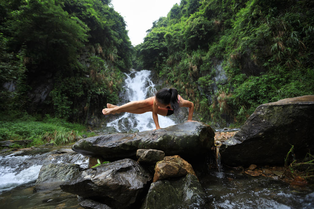 Молода жінка практикує йогу біля водоспаду в лісі
 - Фото, зображення