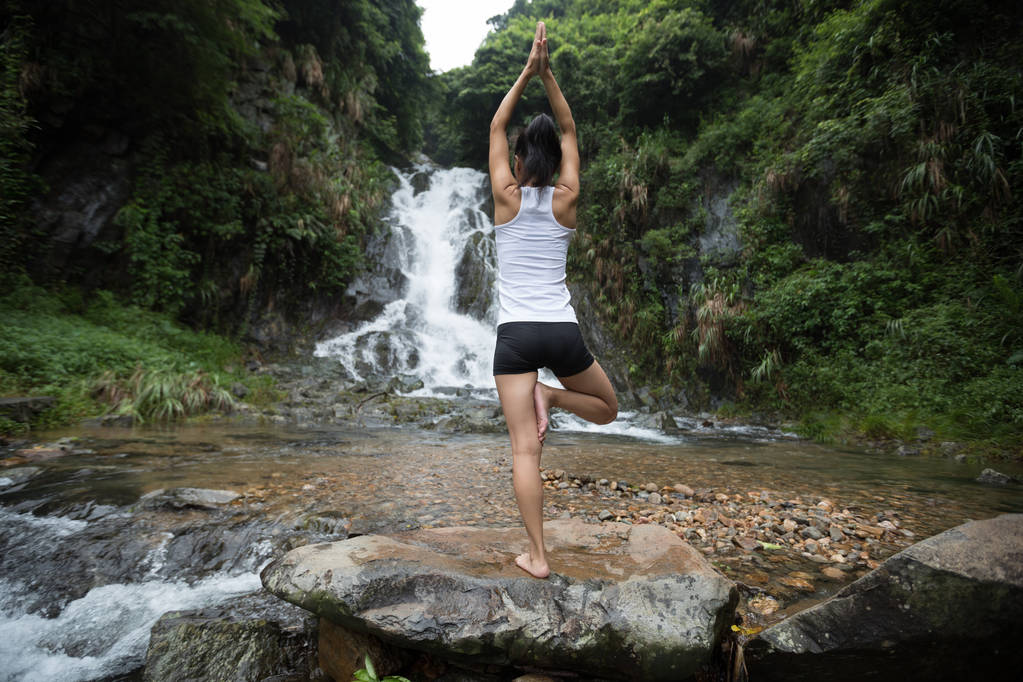 Jonge vrouw beoefenen van yoga in de buurt van de waterval in bos - Foto, afbeelding