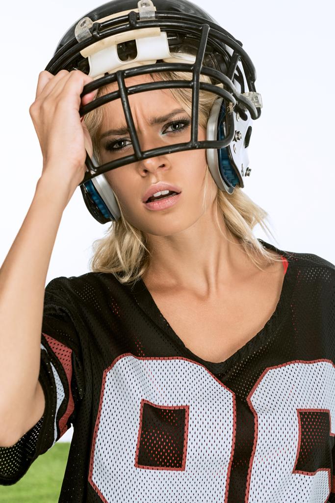 close-up portrait of exhausted young woman in american football uniform taking off helmet isolated on white - Photo, Image