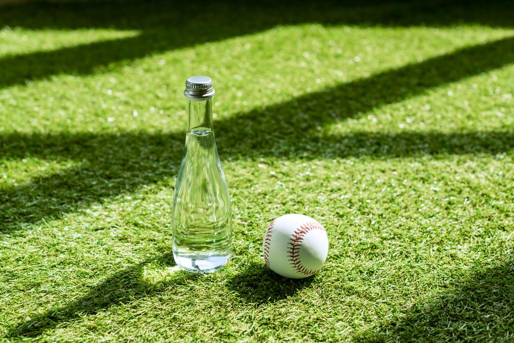 glass water battle with baseball ball lying on green grass - Photo, Image
