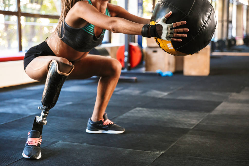 Porträt der schönen invaliden Frau mit Prothese im Trainingsanzug beim Sit-Ups mit Fitnessball im Fitnessstudio - Foto, Bild