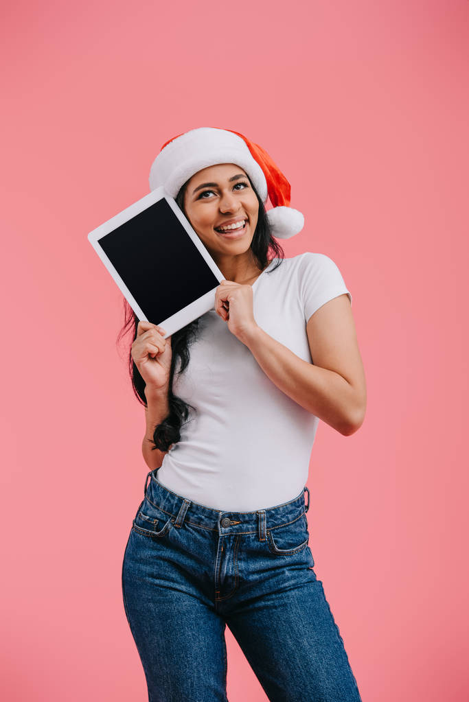 Porträt einer glücklichen afrikanisch-amerikanischen Frau mit Weihnachtsmann-Hut und Tablet mit leerem Bildschirm, isoliert auf rosa - Foto, Bild