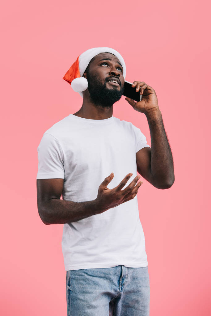 портрет емоційного афроамериканця в капелюсі Санта Клауса, що говорить на смартфоні ізольовано на рожевому
  - Фото, зображення