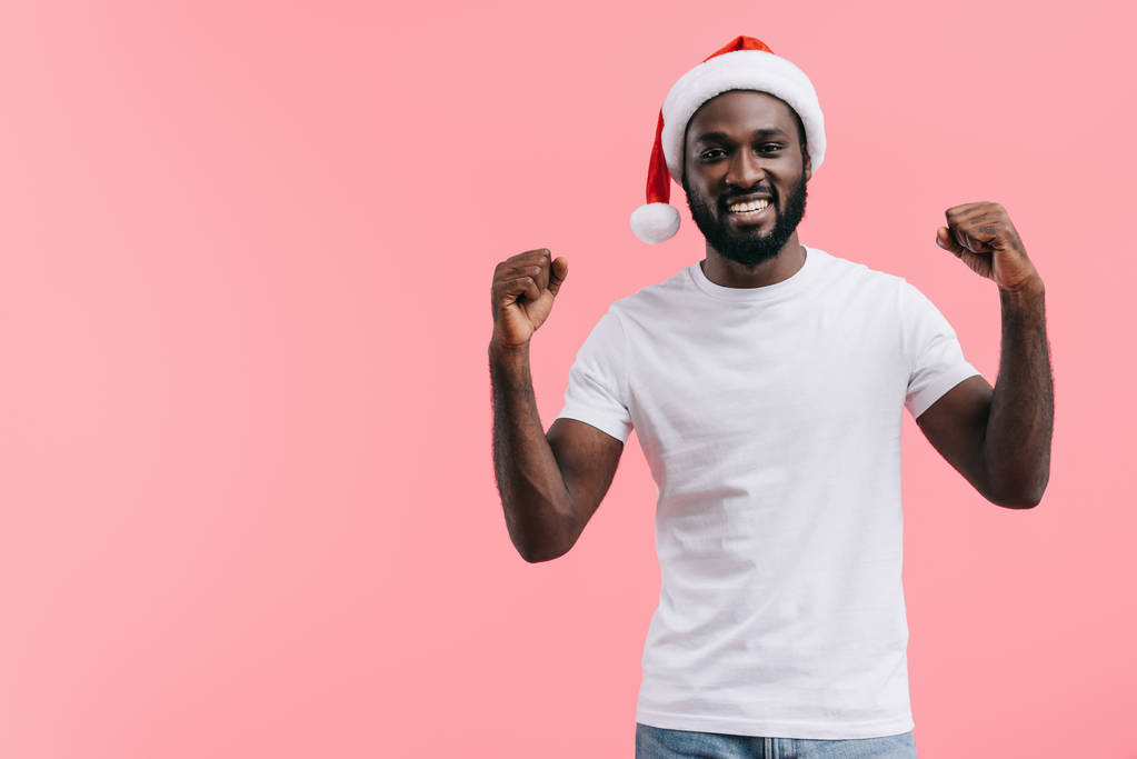 felice uomo afroamericano con braccia alzate in cappello di Natale isolato su sfondo rosa
 - Foto, immagini