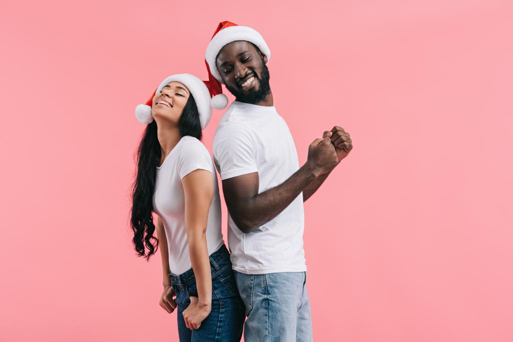 onnellinen afrikkalainen amerikkalainen pari joulun hatut selästä selkään eristetty vaaleanpunainen tausta
  - Valokuva, kuva